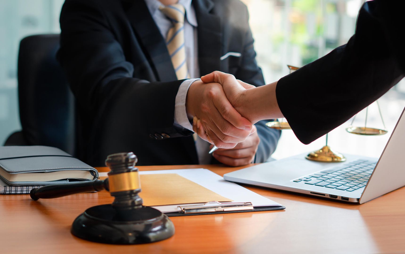 Zwei Personen in Anzügen geben sich an einem Schreibtisch die Hand